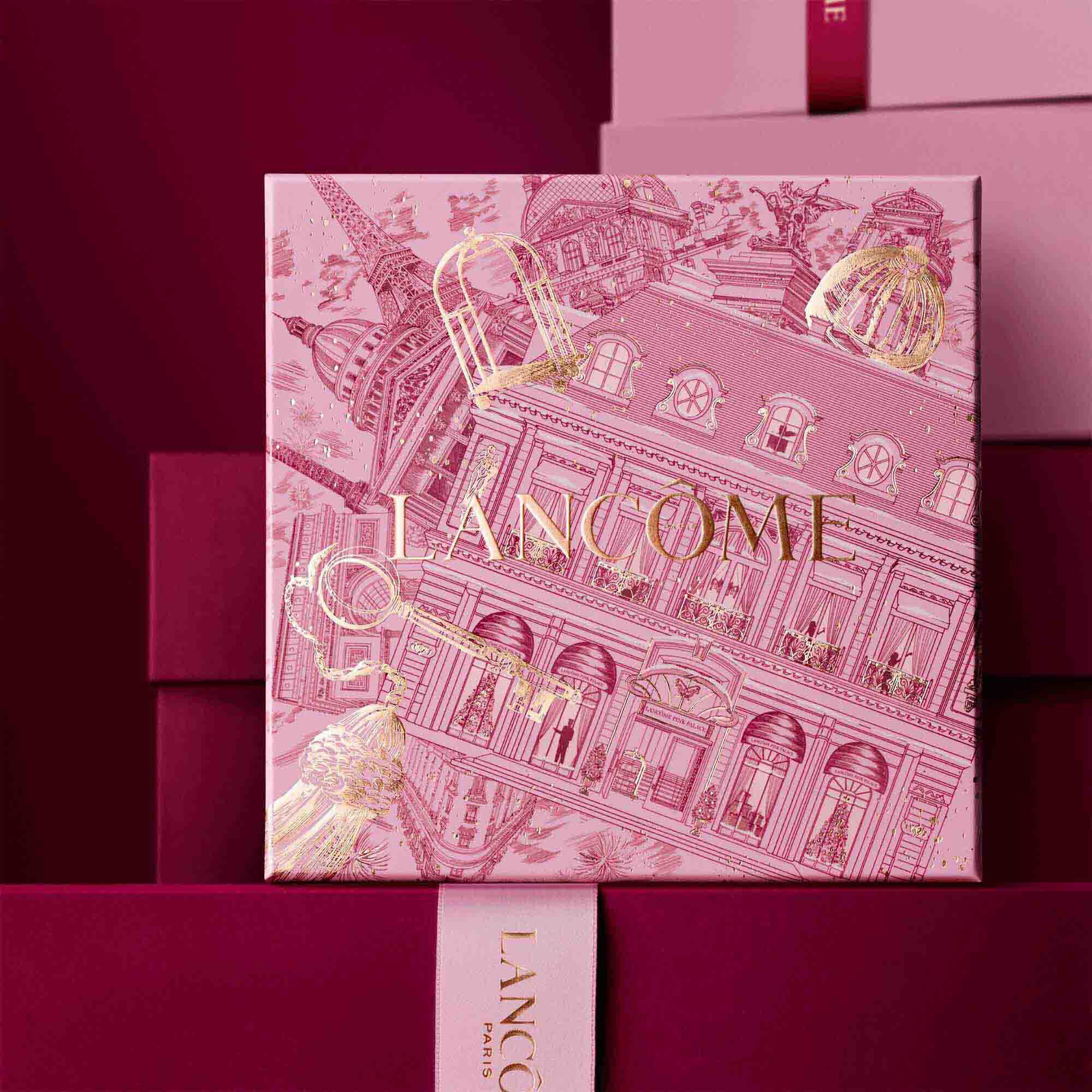 Image of pink Lancome holiday gift box standing in front of a pile of pink and dark red gift boxes, set against a dark red background.