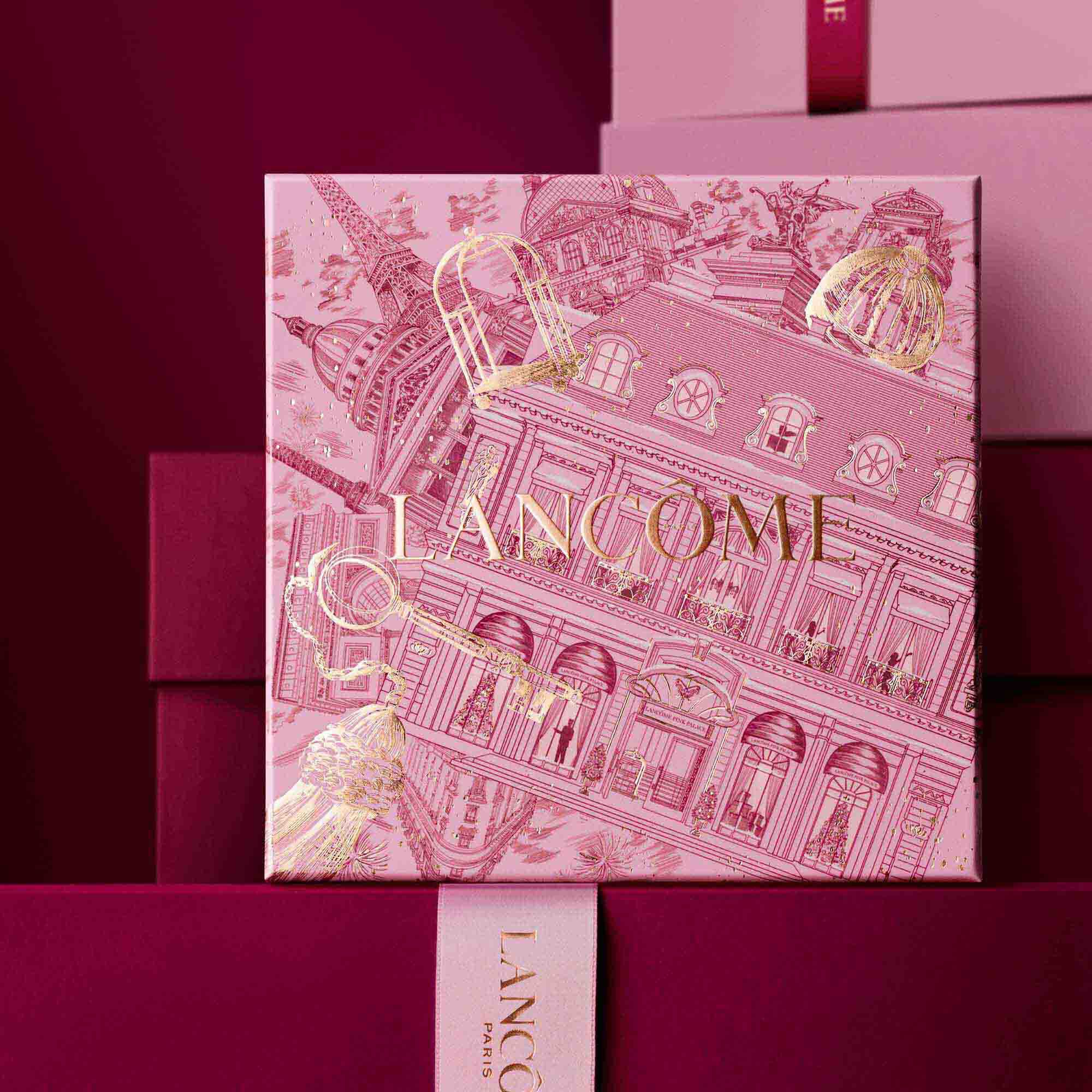 Image of pink Lancome holiday gift box standing in front of a pile of pink and dark red gift boxes, set against a dark red background.