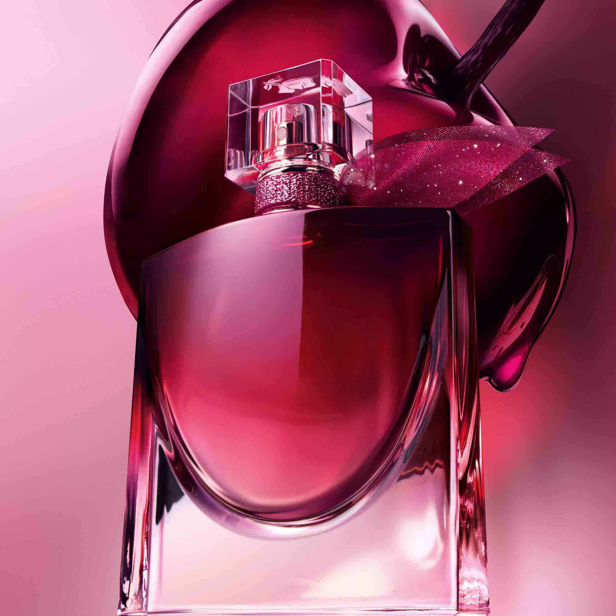 A close-up artistic shot of the burgundy perfume bottle positioned in front of a large, glossy dark cherry.	