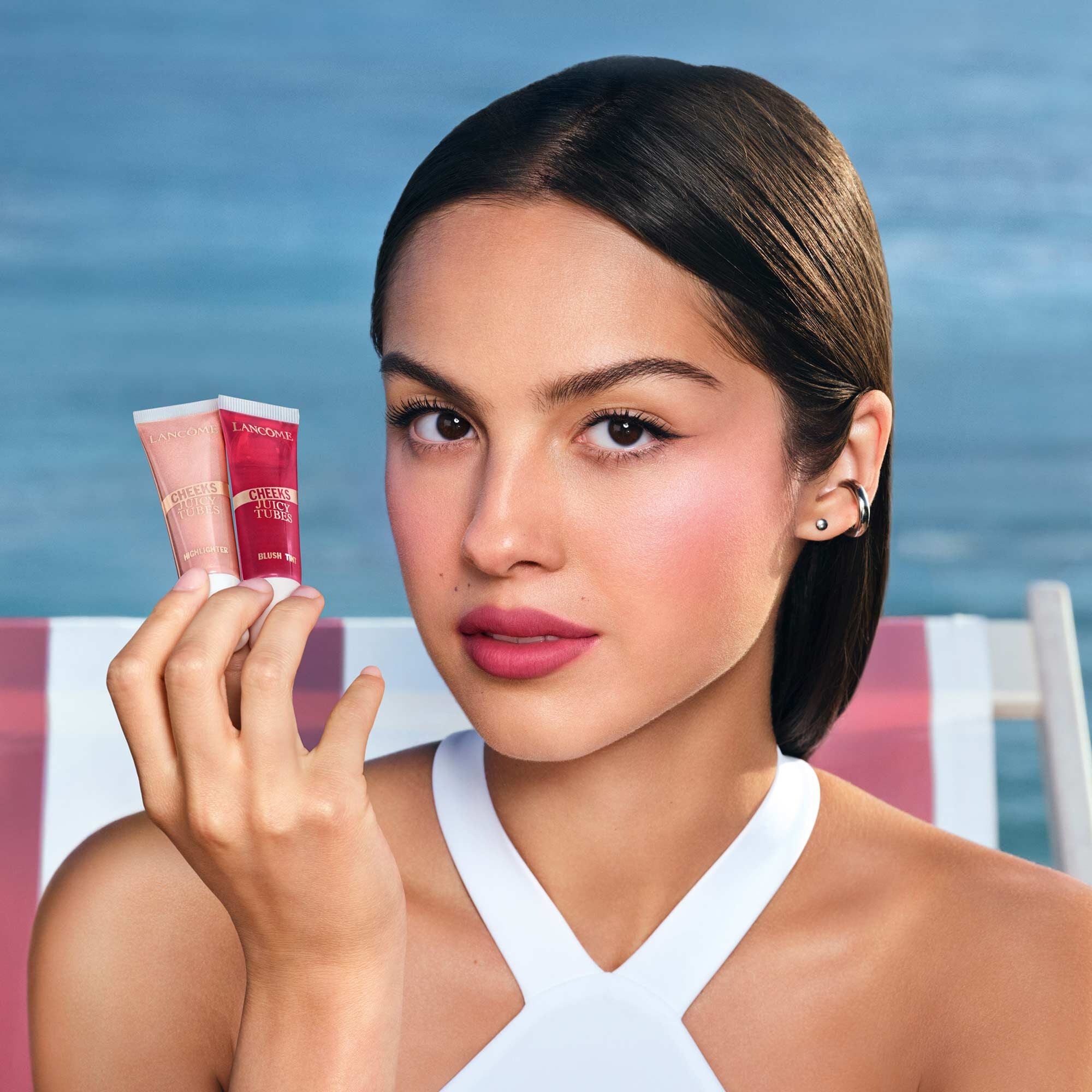 Olivia Rodrigo holding a Juicy Tubes Highlighter with a beach background.