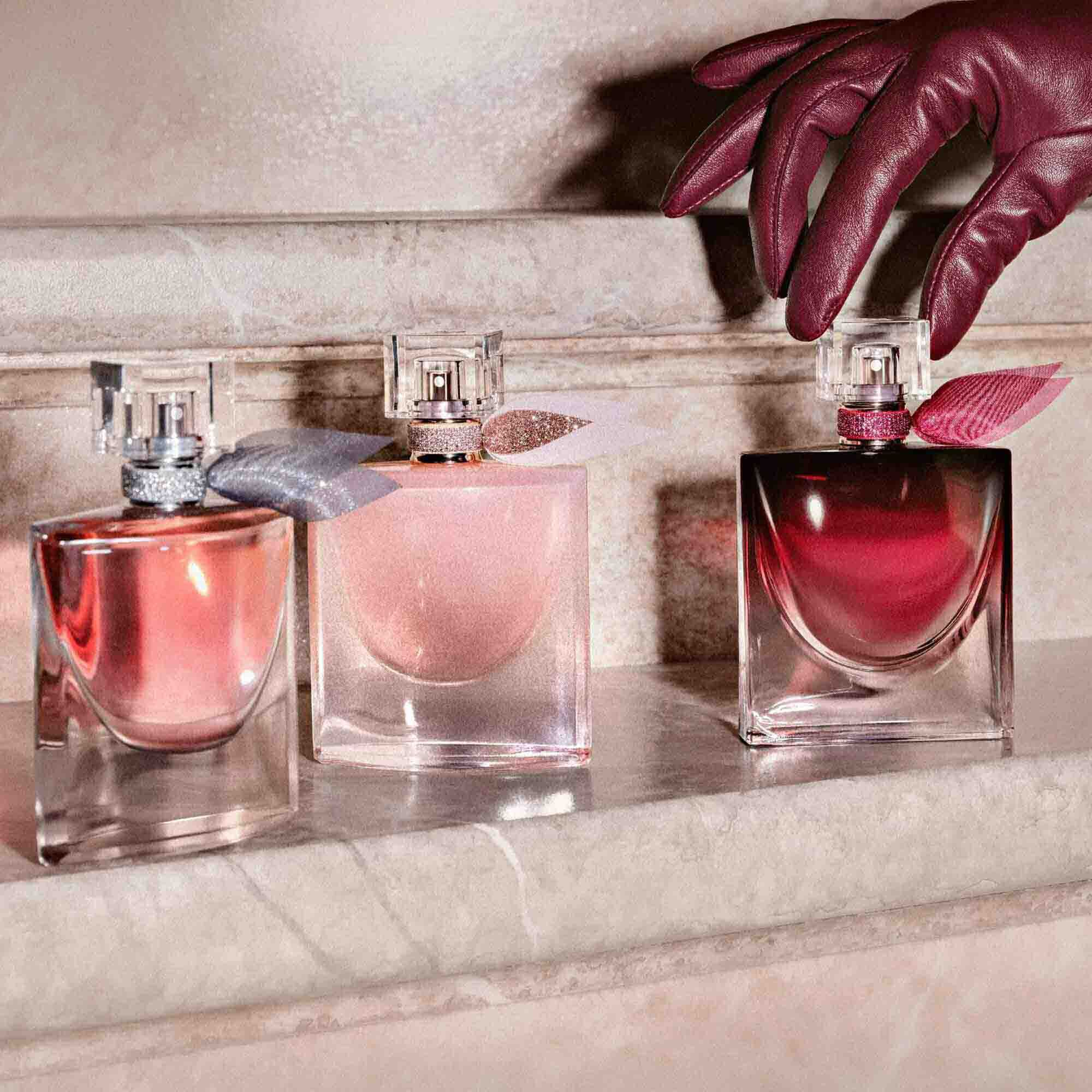 Three different versions of La Vie Est Belle in varying shades of pink and burgundy are lined up on a stone step being reached for by a hand in a leather glove.	