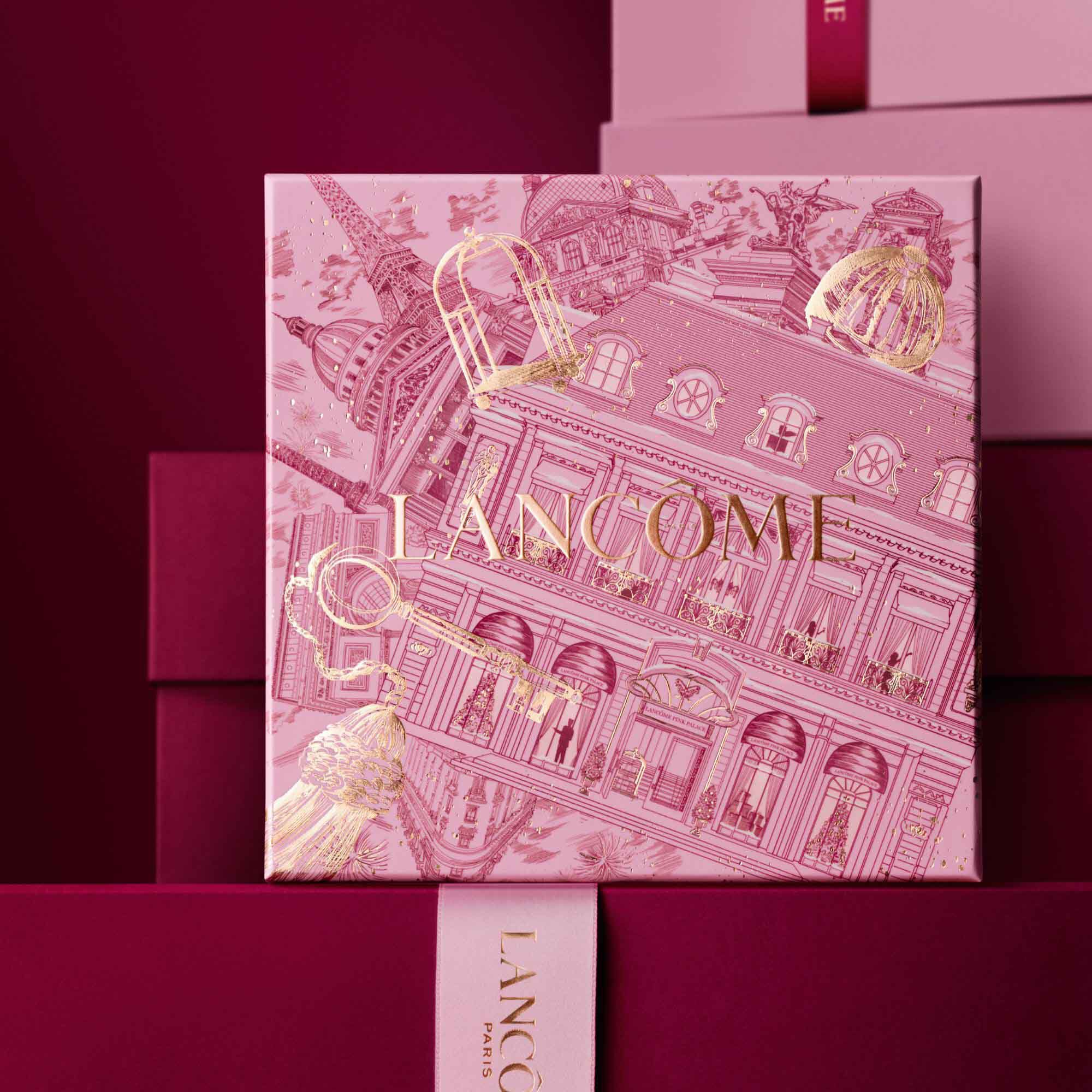 Image of pink Lancome holiday gift box standing in front of a pile of pink and dark red gift boxes, set against a dark red background. 