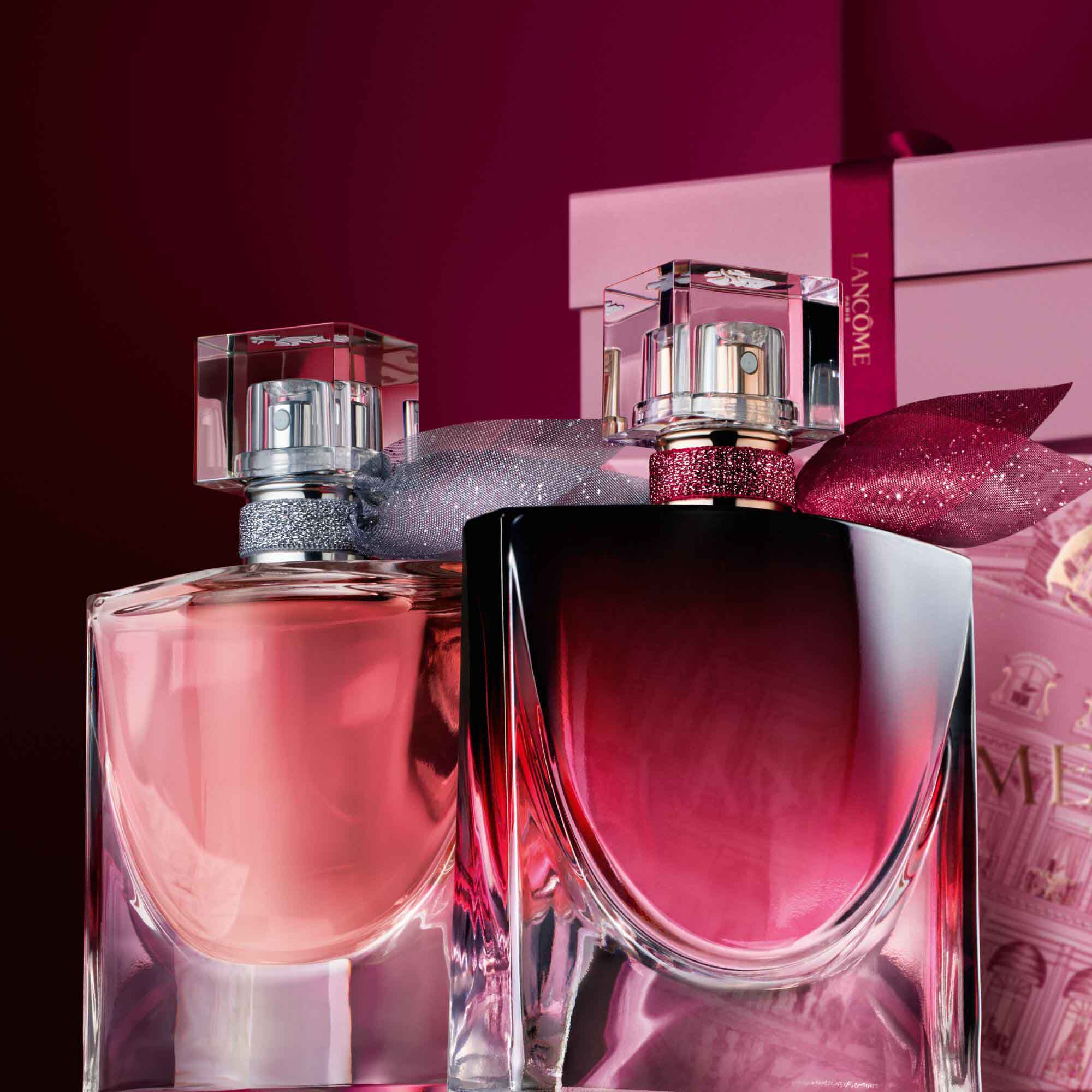 Image of La vie est belle EDP and La vie est belle L'Elixir Very Cherry standing in front of a pile of pink and dark red gift boxes, set against a dark red background. 