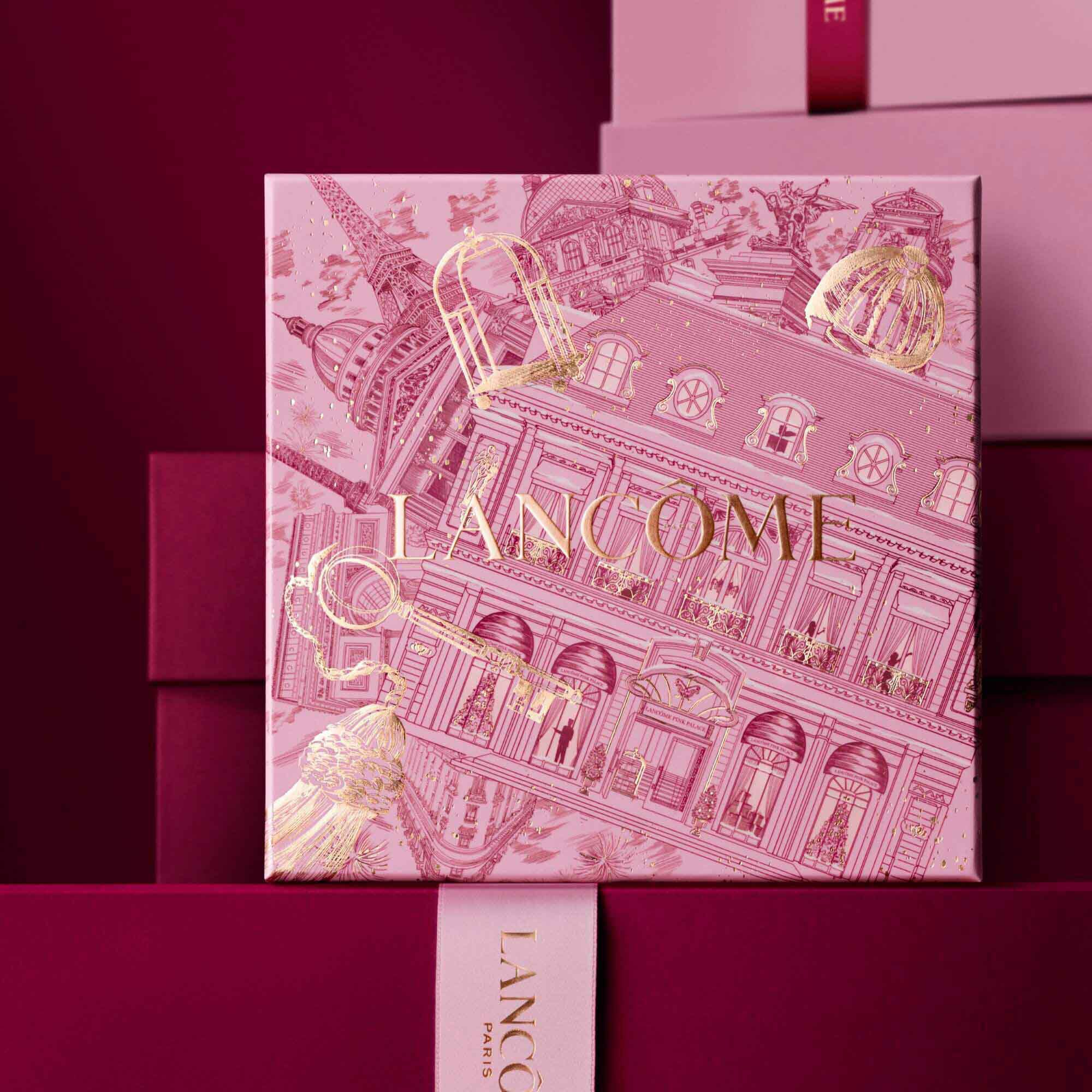 Image of pink Lancome holiday gift box standing in front of a pile of pink and dark red gift boxes, set against a dark red background. 